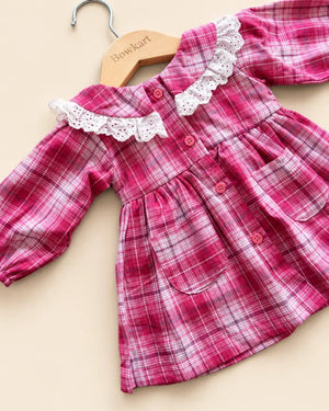 Pink plaid girls' frock with white lace collar, long sleeves, buttons, and front pockets