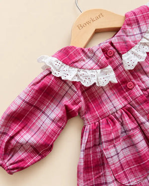 Pink plaid girls' frock with white lace collar, long sleeves, buttons, and front pockets