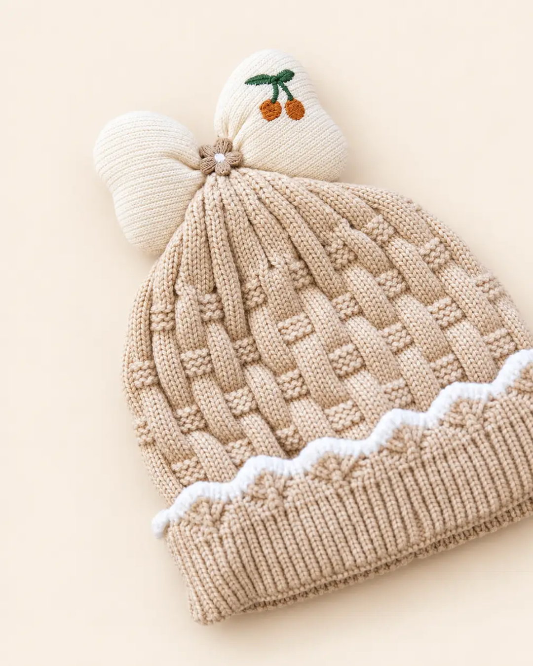Knitted baby beanie with bow detail, cherry embroidery, and scalloped trim
