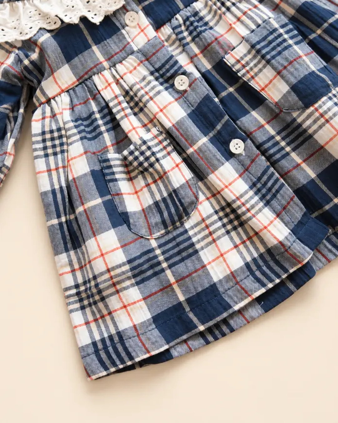 Navy blue plaid girls' frock with eyelet lace collar, long sleeves, buttons, and front pockets