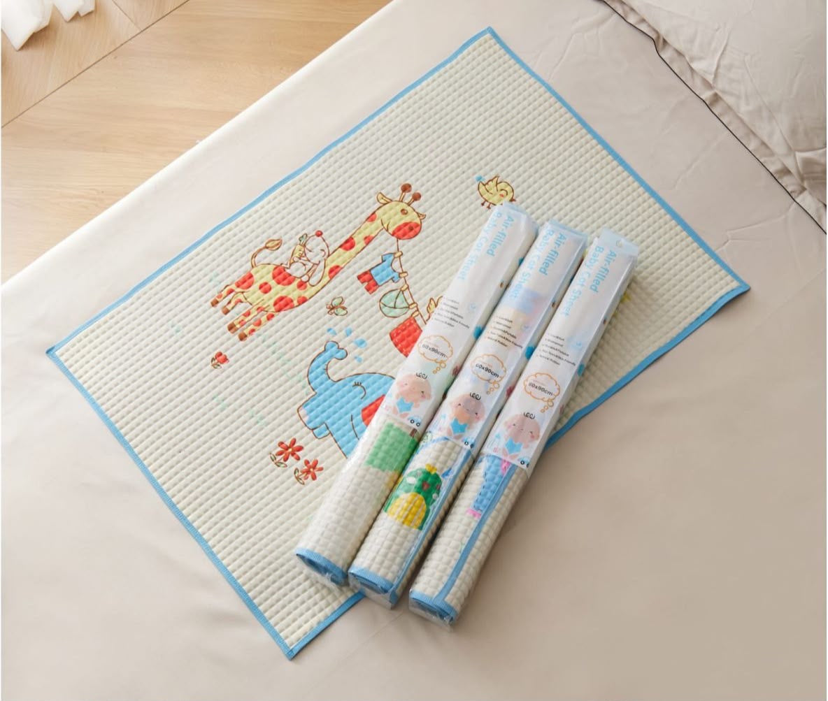 A rectangular baby play mat with a waffle texture, blue border, and colorful cartoon animal illustrations, shown on a bed with three rolled-up versions of the same mat.