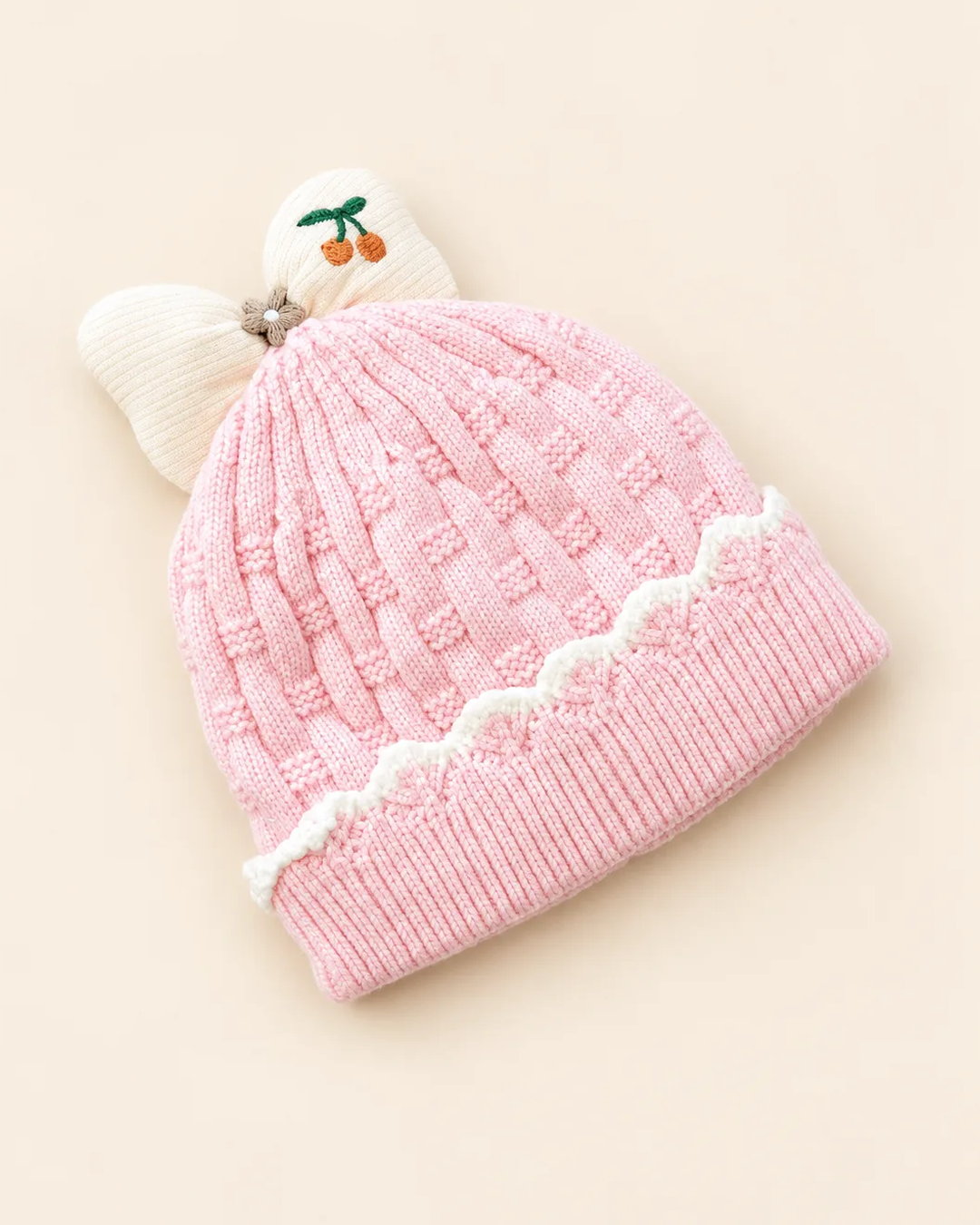 Knitted baby beanie with bow detail, cherry embroidery, and scalloped trim