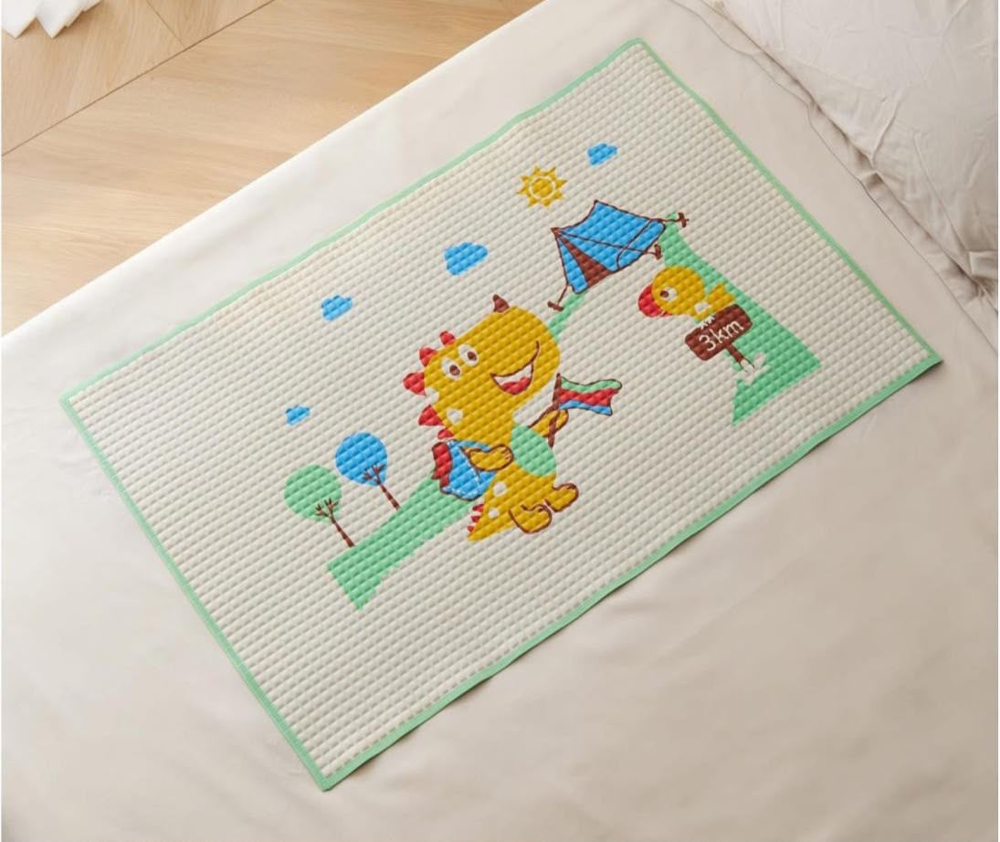 A rectangular white textured mat with a mint green border and a colorful cartoon camping scene, placed on a white bed over a light wood floor.